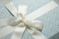Preview: Die Brautkleidbox Blue Flower Dream wird mit einer passenden elfenbeinfarbenen Satinschleife kombiniert.