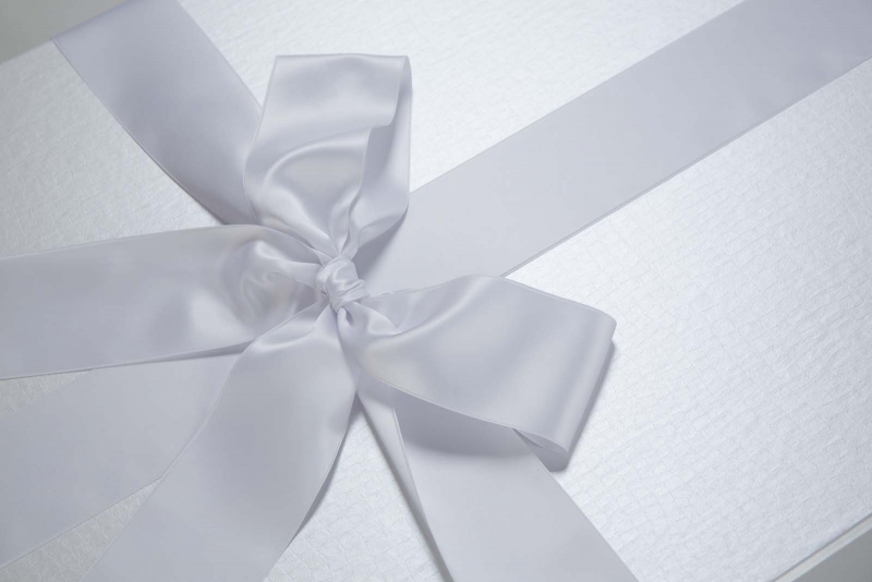 Die Brautkleidbox Pearly Croco wird mit einem weißen Satinband gebunden.