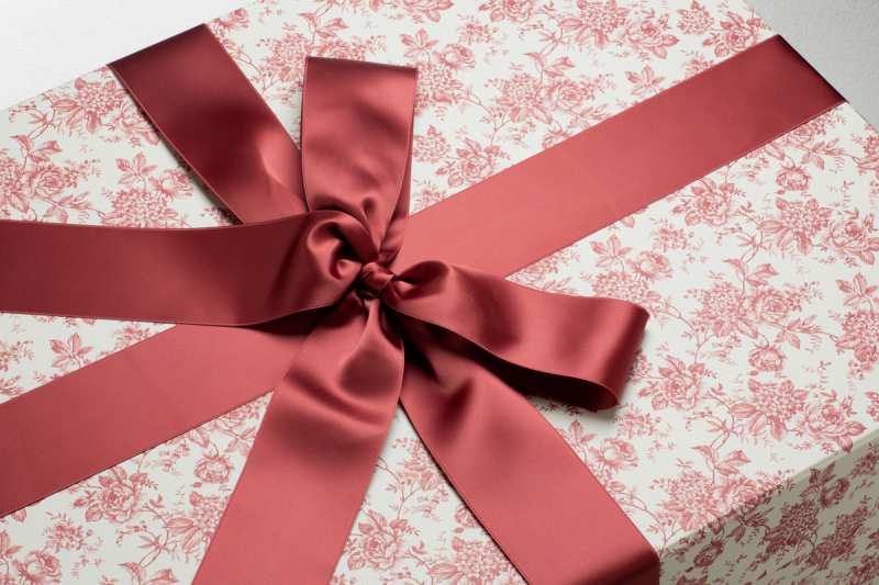 Die Brautkleidbox Red Vintage Flowers wird mit einem passenden bordeaux-roten Satinband gebunden.